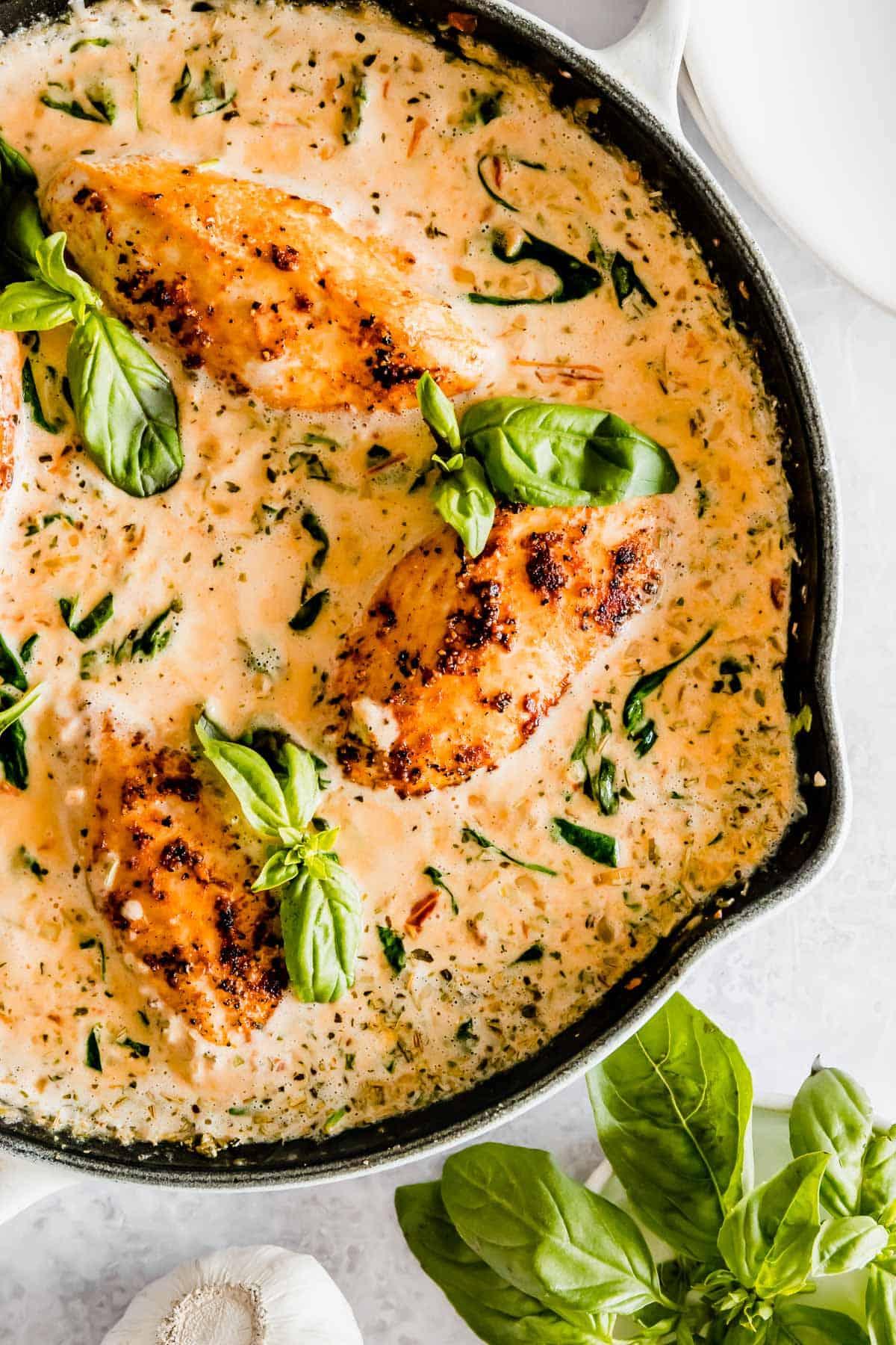 Creamy Tuscan Chicken in a skillet, garnished with fresh herbs and parmesan cheese