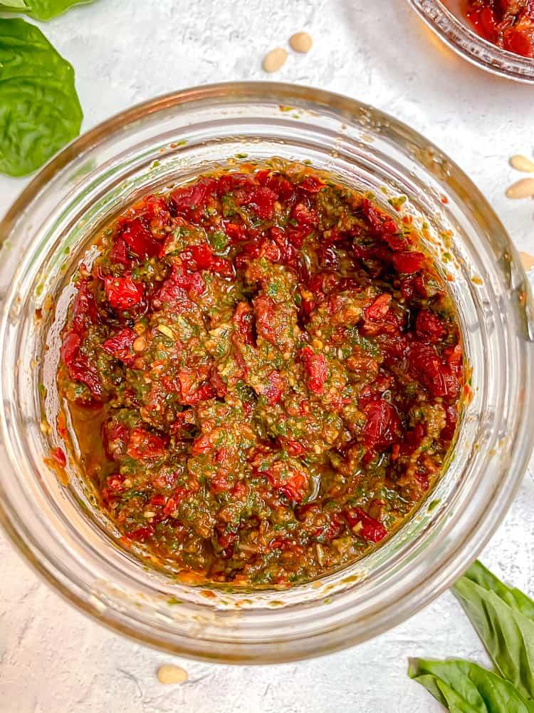 A close-up shot of a bowl of chopped sun-dried tomatoes and fresh basil leaves.