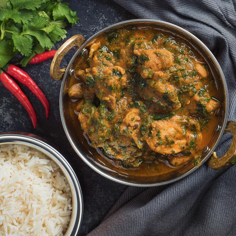 Close-up shot of a vibrant Chicken Saag in a rustic bowl, garnished with fresh cilantro