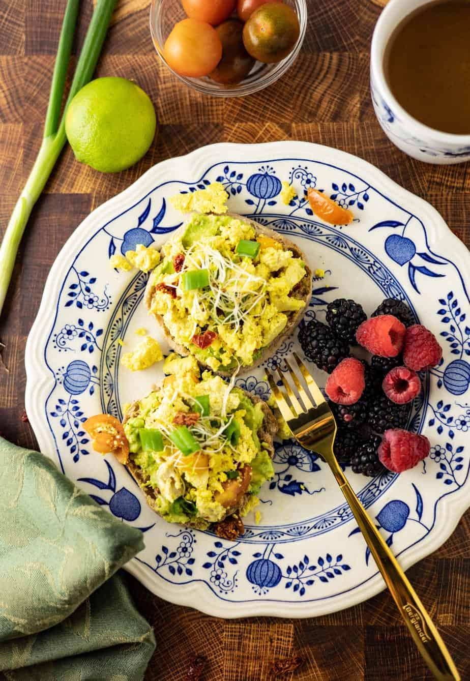 A bowl of creamy avocado tofu scramble garnished with fresh herbs and a side of whole wheat toast