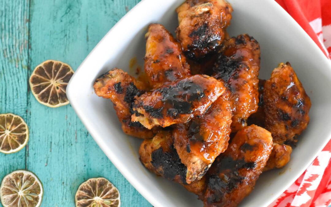 A close up of glistening mango habanero chicken wings being grilled