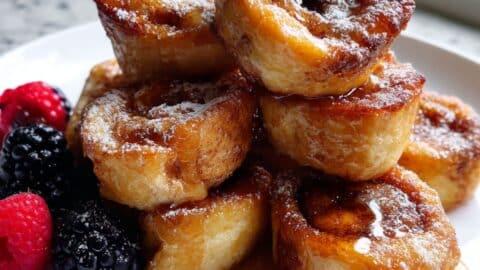 hand drizzling white glaze over cinnamon roll french toast bites