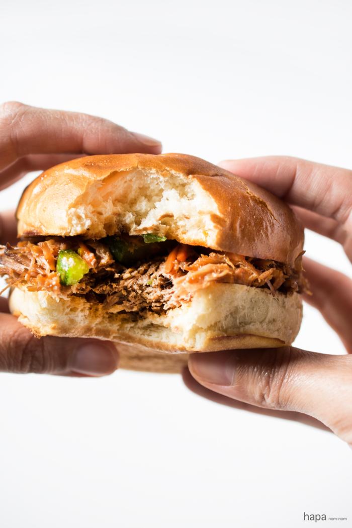person serving slow cooker korean bbq pulled pork on a bun with toppings