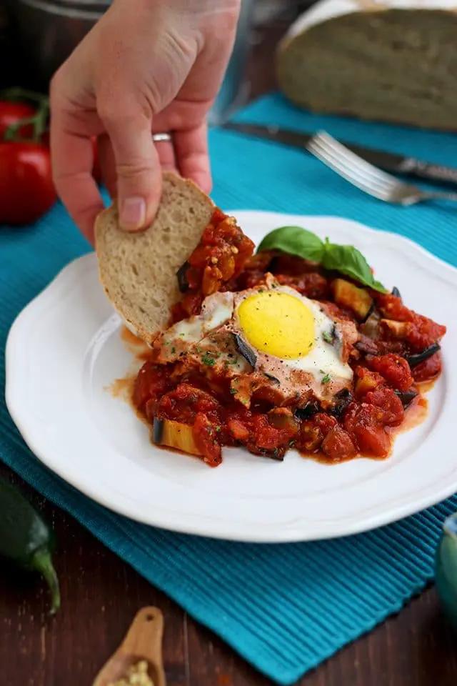 A person dipping a piece of crusty bread into the shakshuka sauce