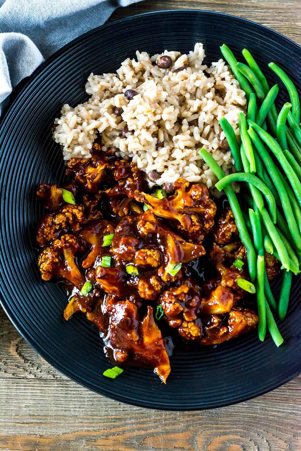 A person serving a plate of Jamaican jerk cauliflower rice with grilled pineapple