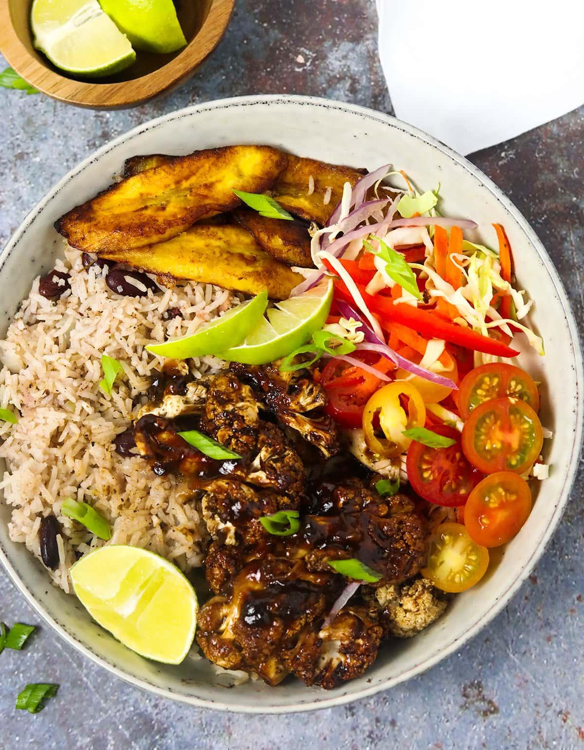 A close-up shot of a colorful bowl of Jamaican jerk cauliflower rice topped with grilled pineapple slices