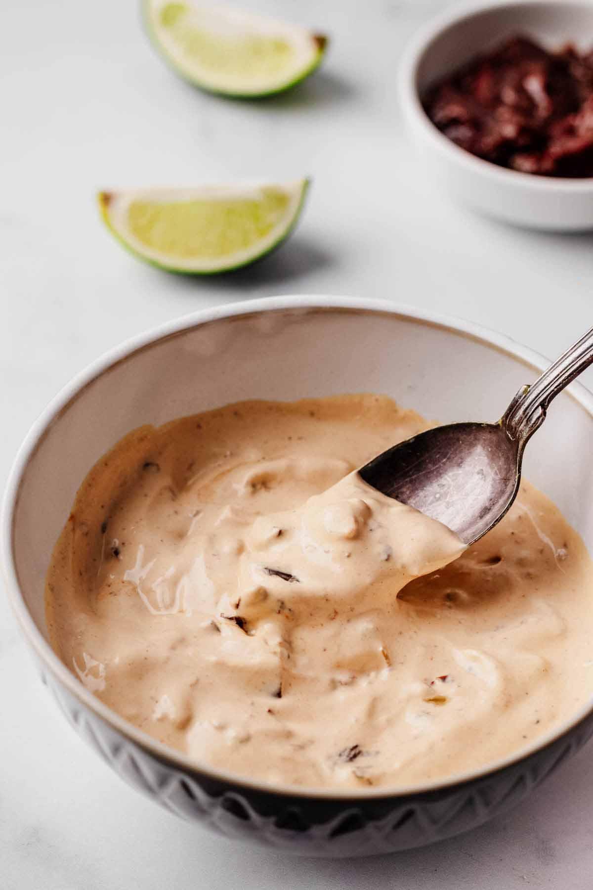 A bowl of creamy, homemade chipotle aioli with a spoon dipping in.