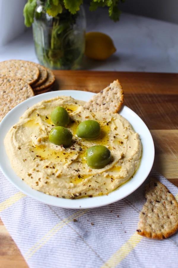 A bowl of creamy Mediterranean hummus with a side of multigrain chips, garnished with fresh herbs and a drizzle of olive oil