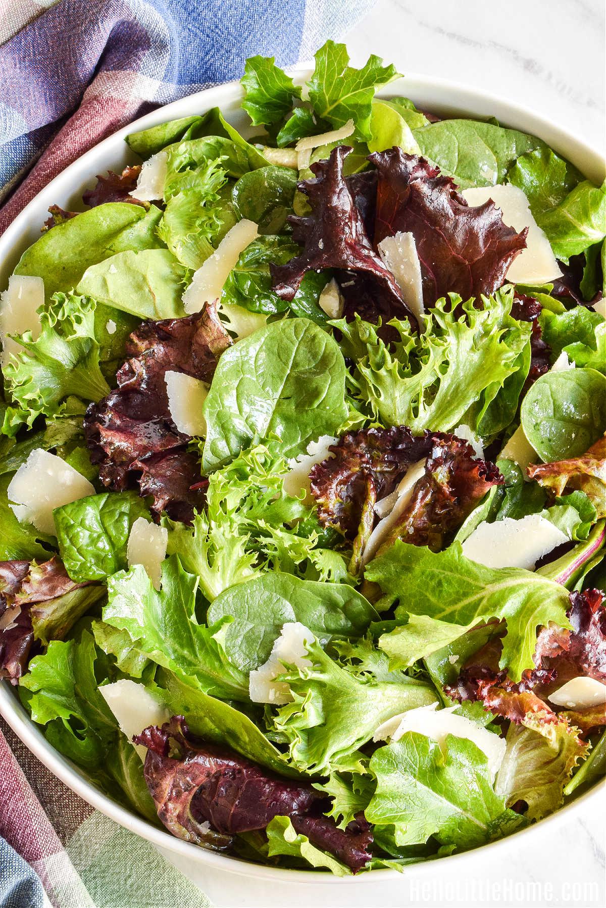 hands sprinkling Rosemary Parmesan Cashews on top of a green salad