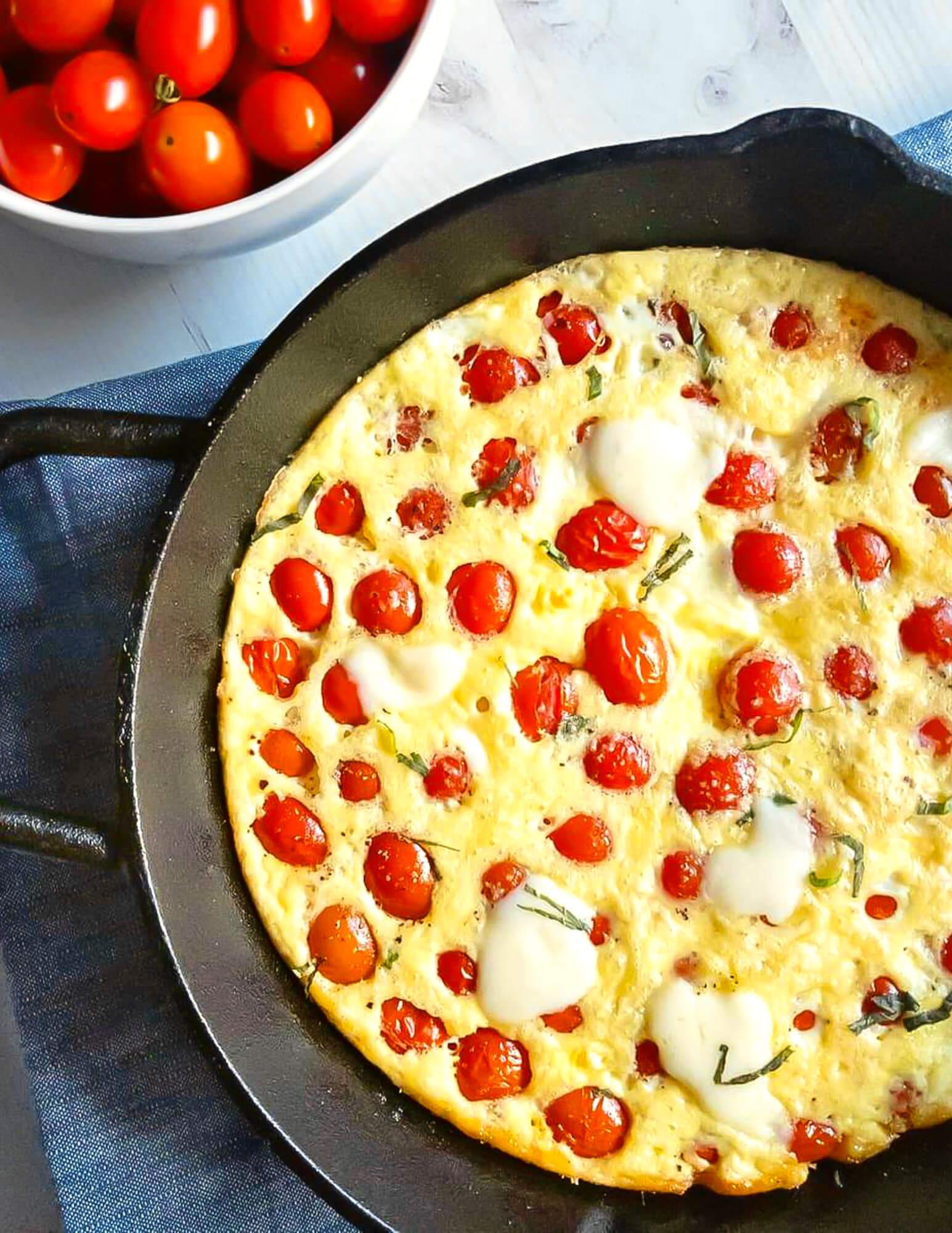 A close-up of a cherry tomato and burrata frittata being taken out of the oven