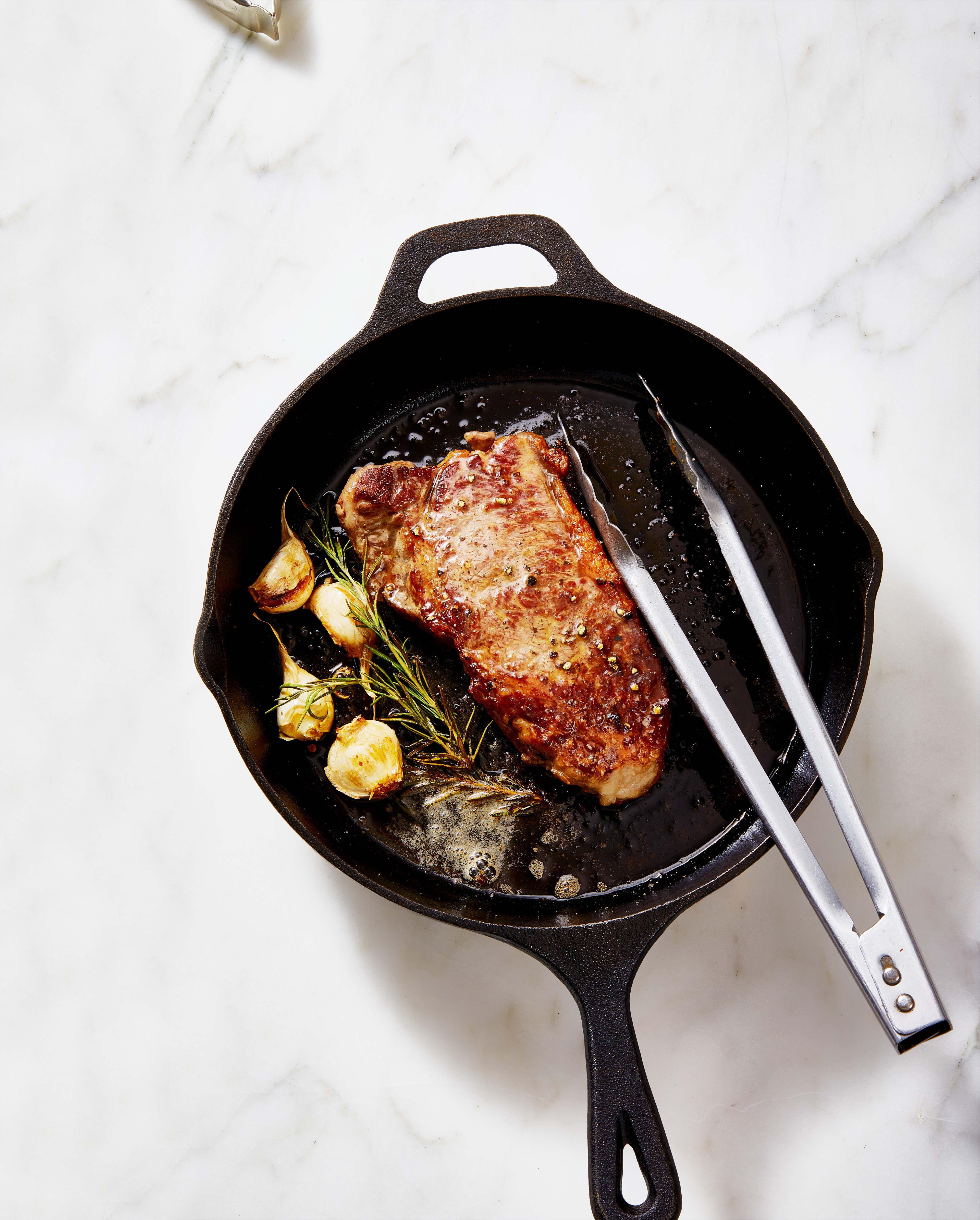 A sizzling New York strip steak in a cast iron skillet
