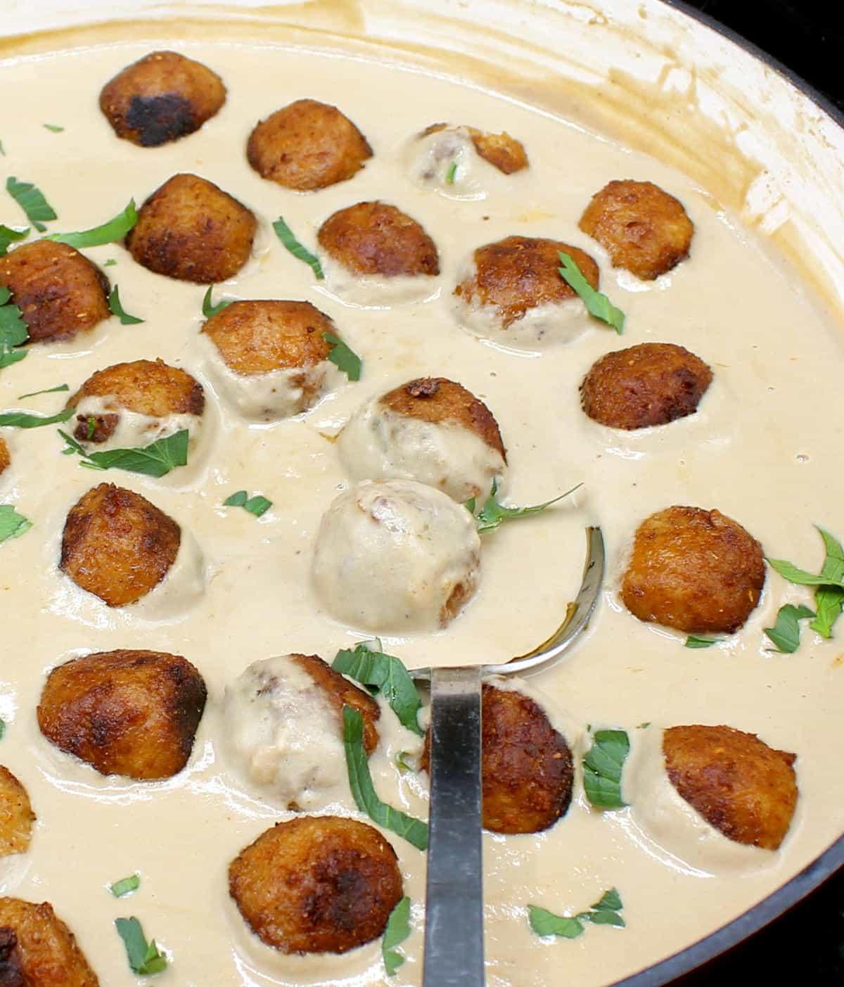 Close-up shot of plant-based meatballs in creamy Caesar dressing, garnished with fresh parsley