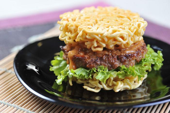 A close-up shot showcasing the layering of the Pork Ramen Burger: the soft bun, juicy pork patty, flavorful ramen broth, and optional toppings.