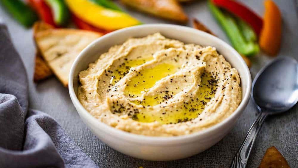 A person carefully drizzling olive oil over a bowl of hummus