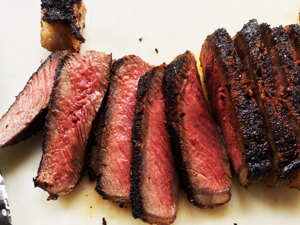 Close-up shot of a coffee-rubbed New York strip steak, perfectly seared and cooked to medium-rare, on a rustic wooden cutting board with fresh herbs sprinkled around