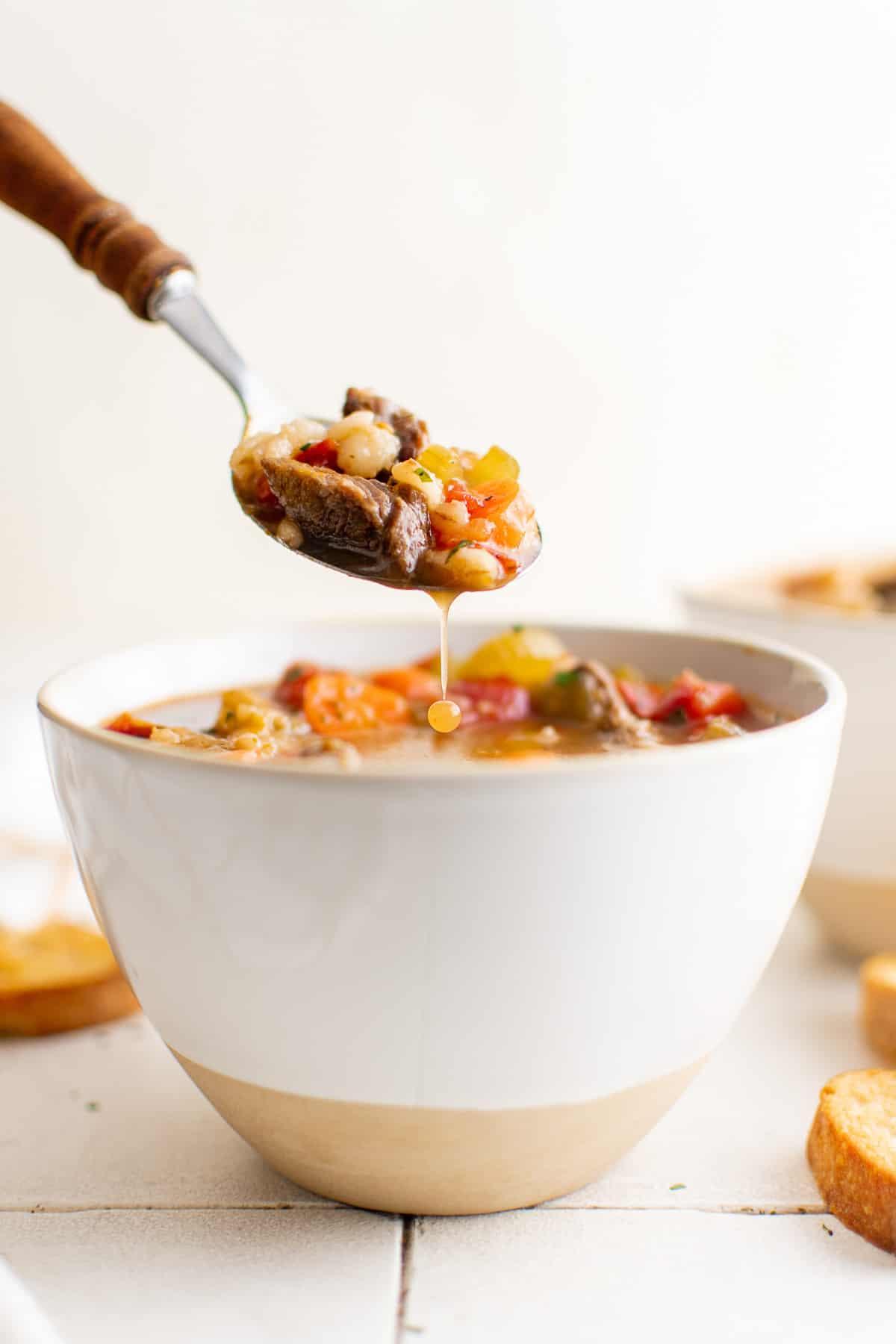 a steaming bowl of beef and barley soup with a spoon