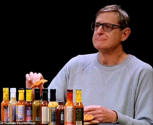 A person holding a honey sriracha wing, sauce dripping slightly, with a blurred background of people enjoying food and drinks.