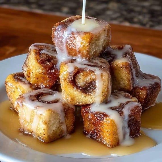 close-up of golden brown cinnamon roll french toast bites stacked on a plate