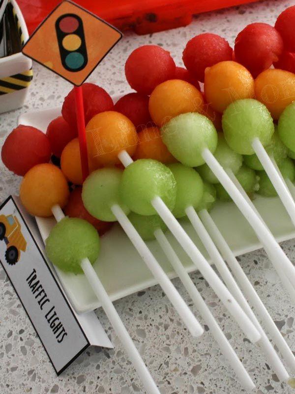 young child smiling at a plate of construction themed fruit skewers