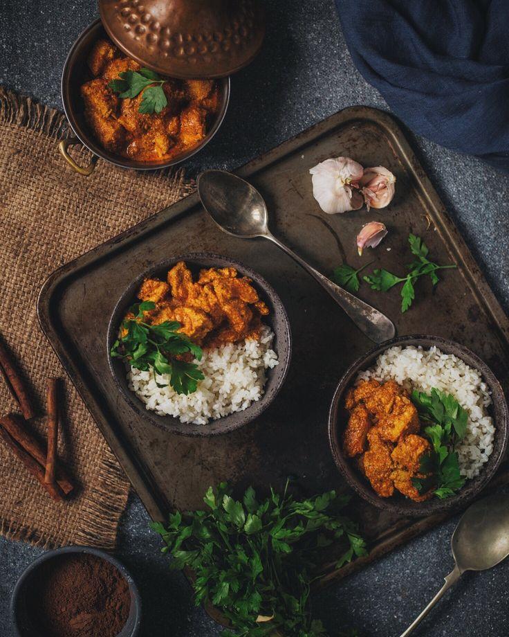 A rustic wooden table setting with a bowl of butter chicken and eggplant, surrounded by other Indian dishes