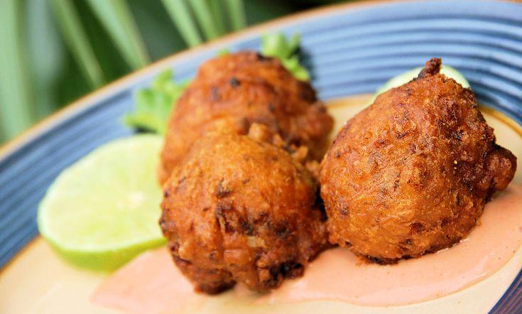 Close up of crispy golden brown conch fritters on a white plate, garnished with lime wedges