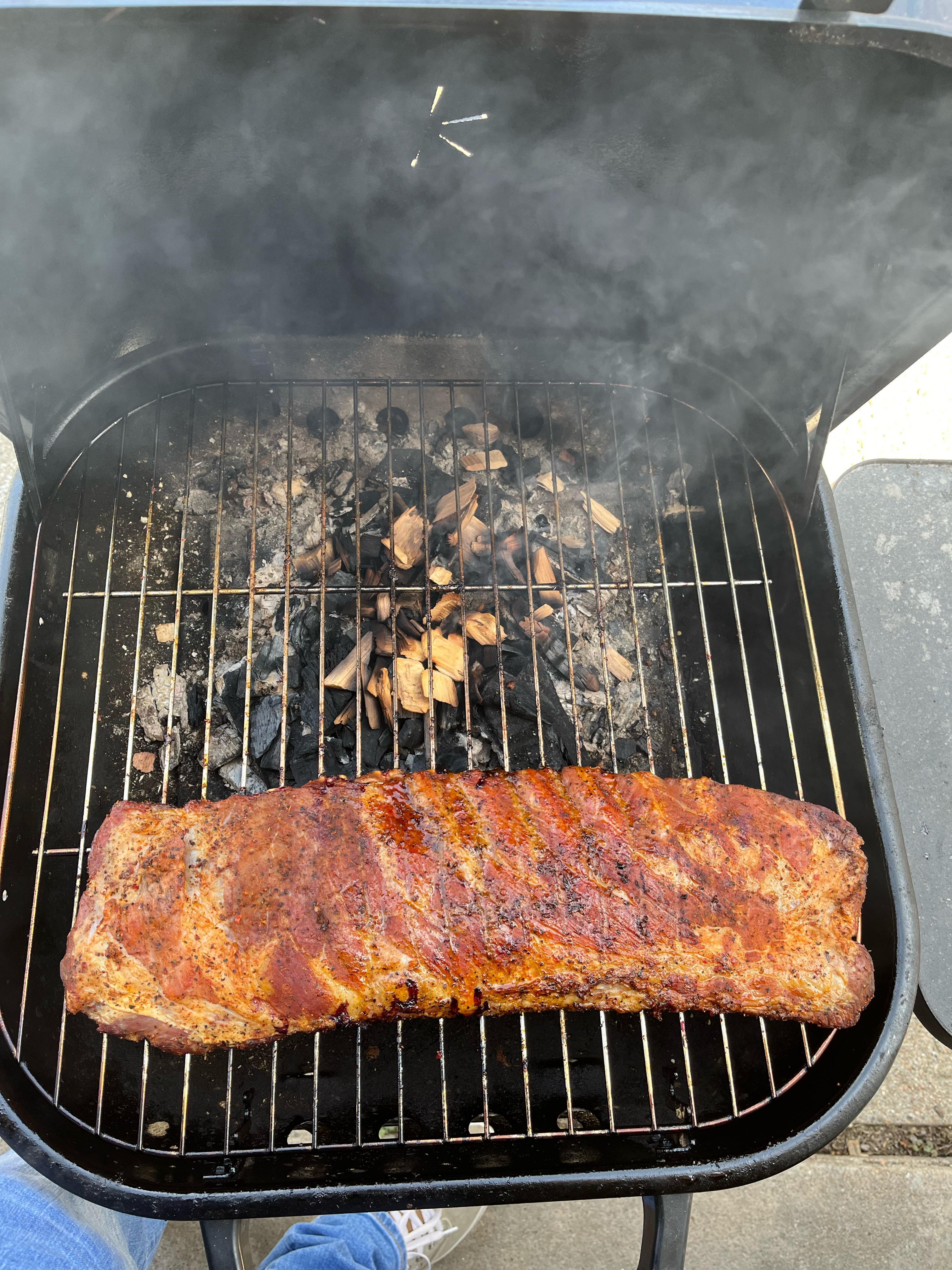 Smoker with ribs inside, surrounded by wood chips and smoking