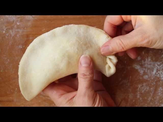 A person's hands carefully shaping and crimping empanada dough