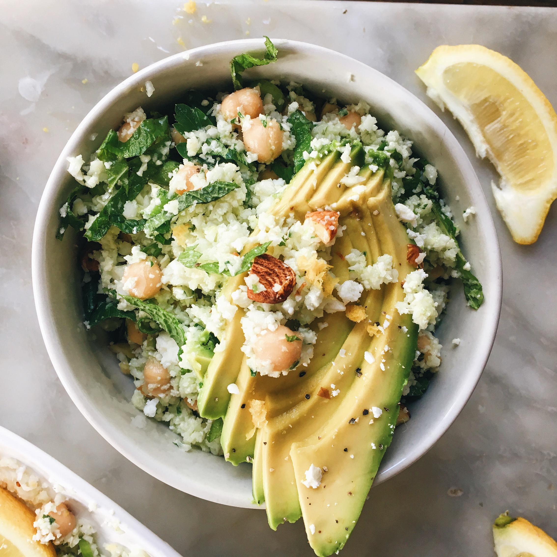 Close-up shot of a vibrant cauliflower rice salad with chickpeas and feta, garnished with fresh herbs and lemon wedges.