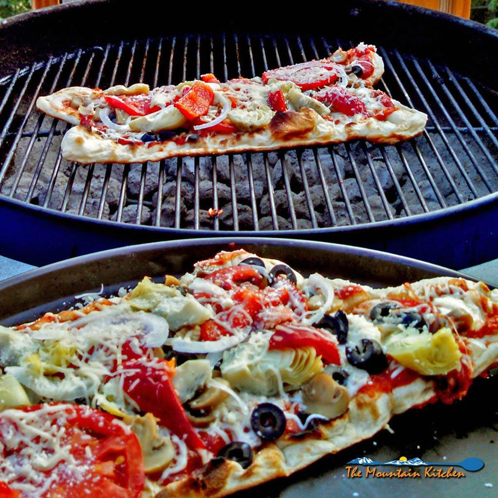 A person placing a grilled vegetable pizza on a grill