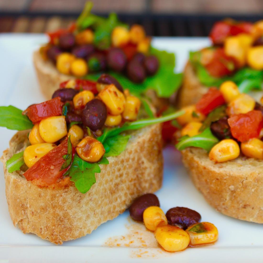 Close-up shot of vibrant bruschetta with black beans, corn, and fresh herbs, garnished with a drizzle of olive oil