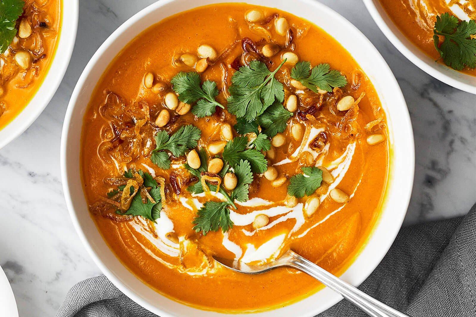 vibrant chilled carrot ginger soup in a bowl, garnished with fresh ginger and cilantro