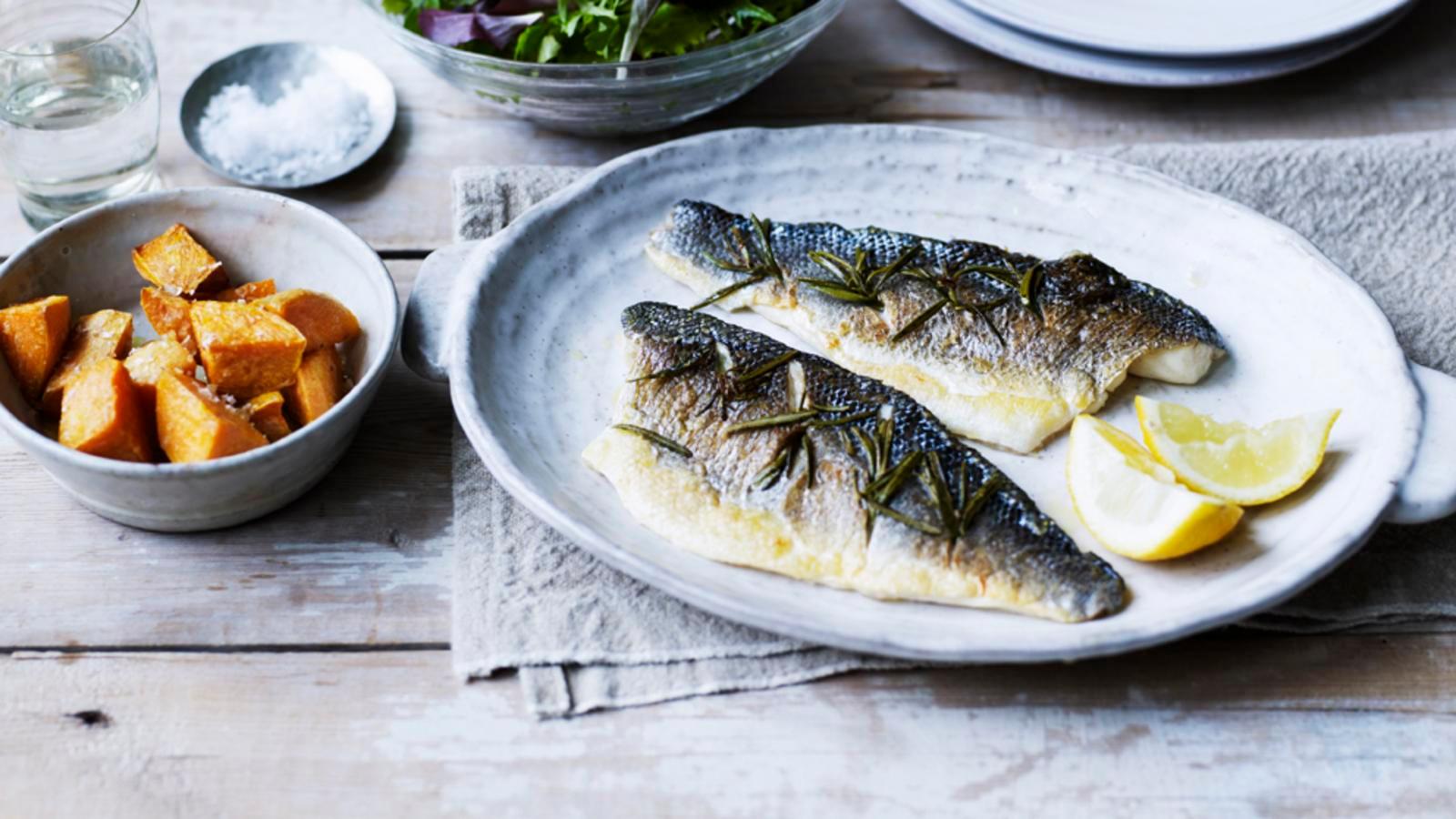 Close-up of a perfectly steamed bass fillet with rosemary and garlic, garnished with lemon