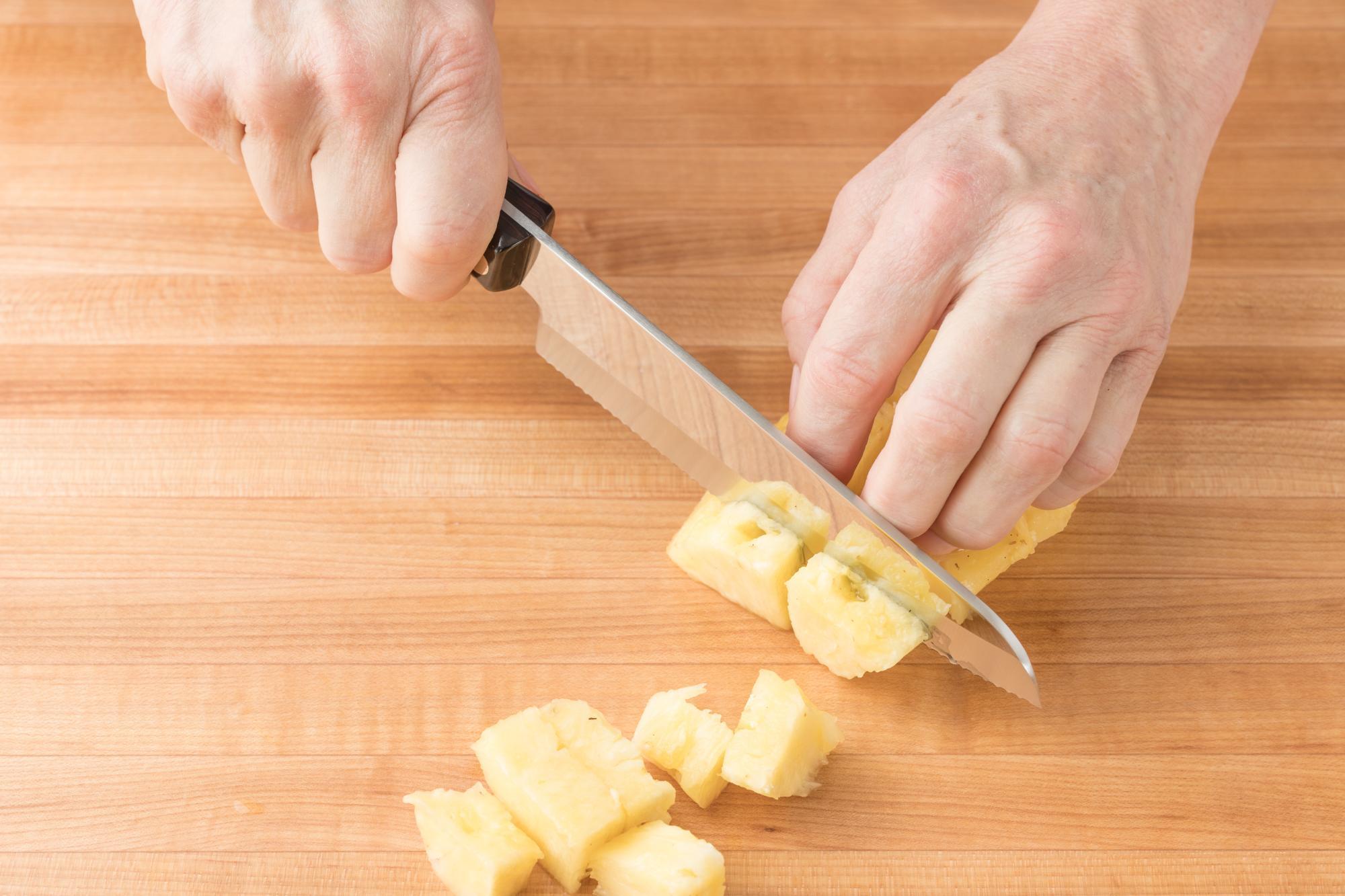 overhead shot of someone preparing pineapple salsa, dicing pineapple on a wooden cutting board