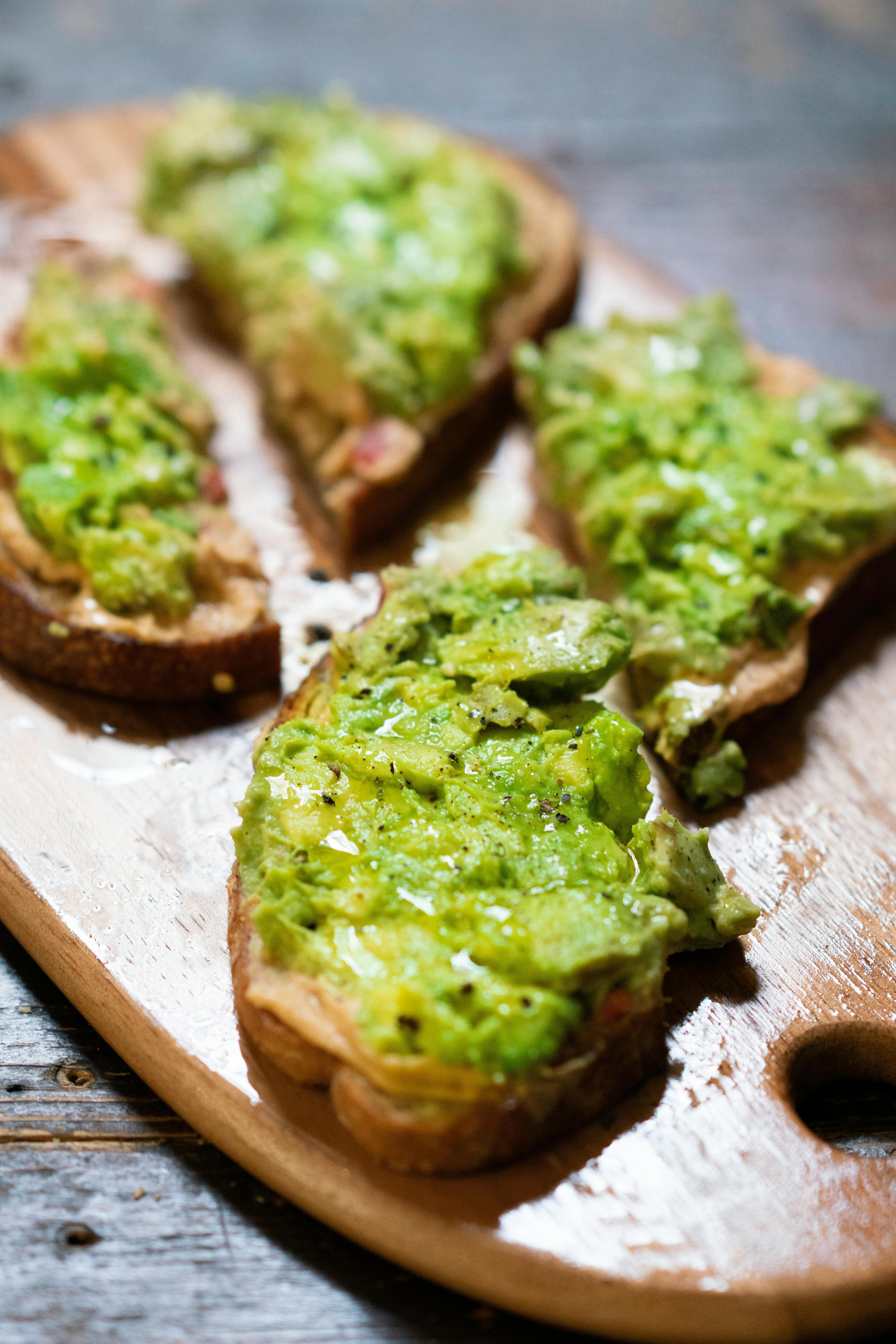 Close up shot of avocado toast with pistachios, sprinkled with salt and pepper on a rustic wooden board.