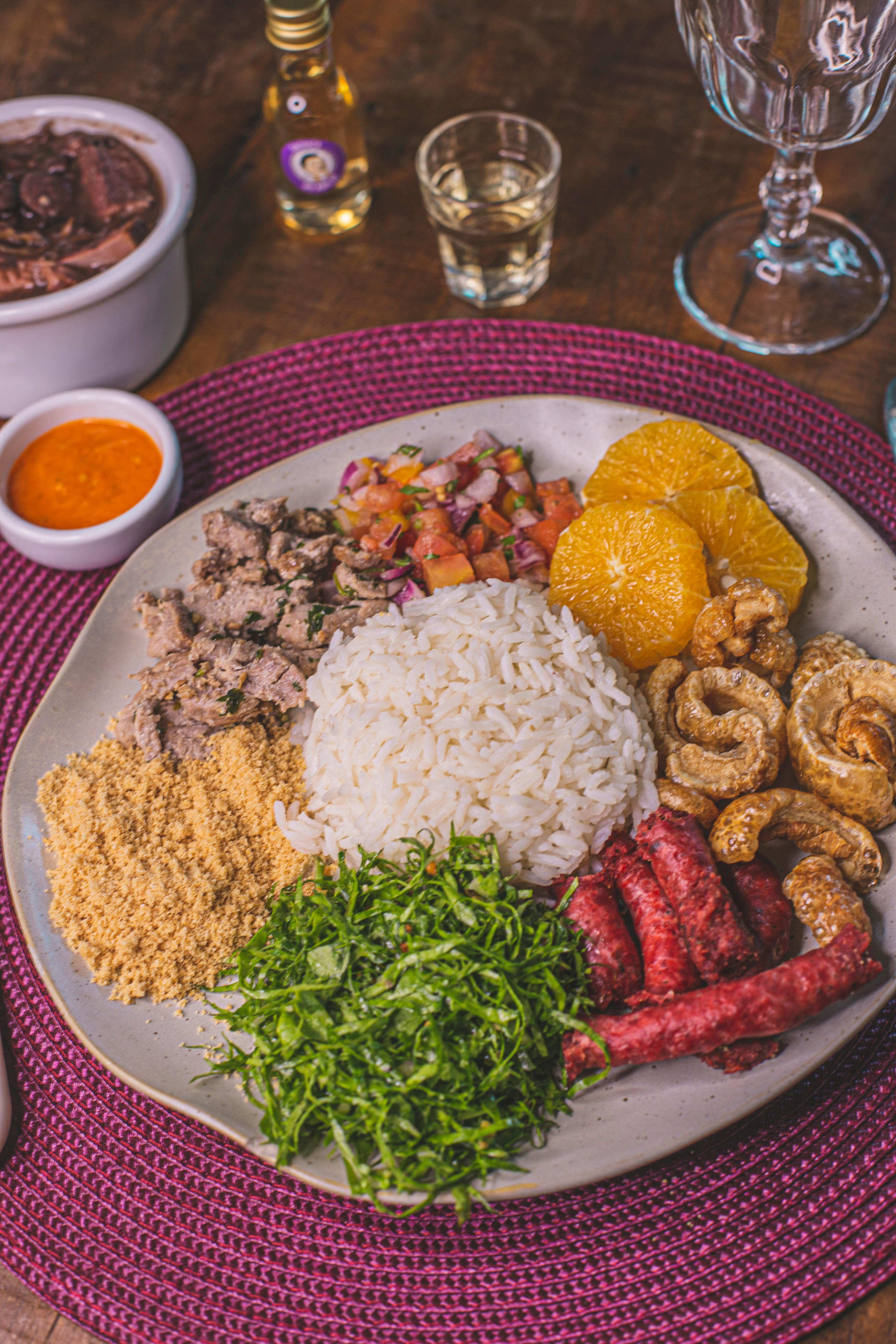 A rustic table set with a steaming bowl of feijoada and a separate plate of sarapatel, garnished with fresh herbs
