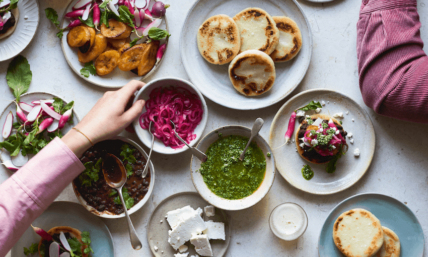 Overhead shot of several Easter Lamb Arepas arranged on a wooden board with bowls of black beans, plantains, and other toppings around them