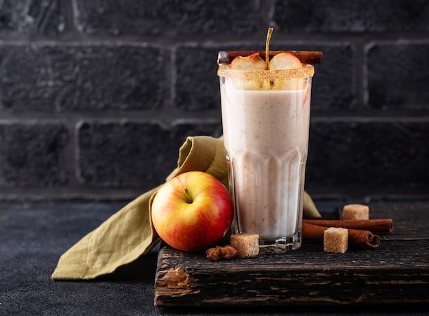 a person holding a glass of apple pie spiced smoothie outside with autumn leaves in the background