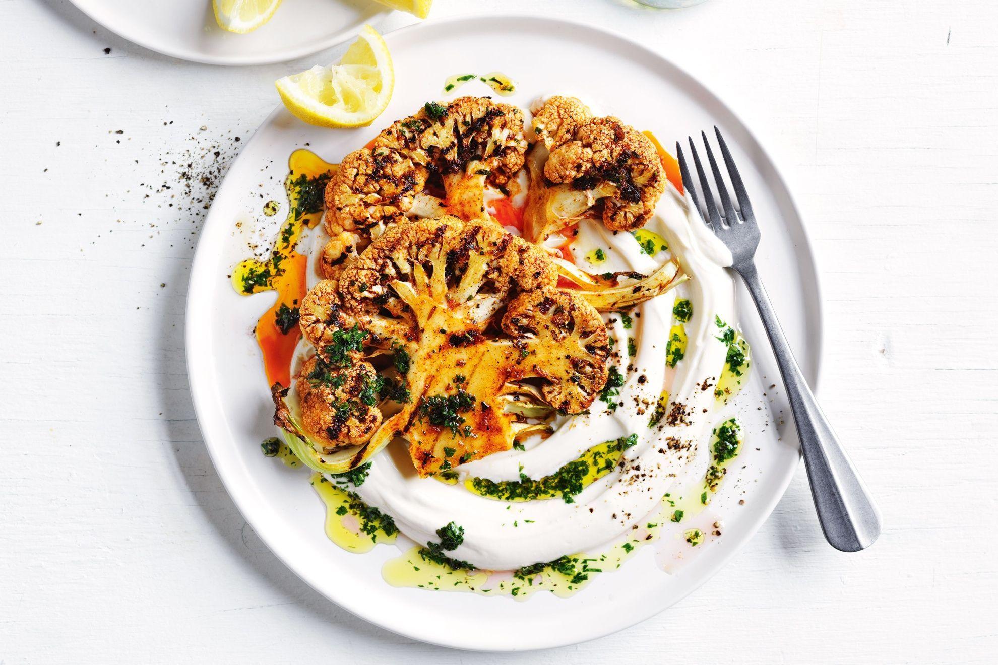 Close-up of perfectly roasted smoked paprika cauliflower steaks topped with melted Manchego cheese, garnished with fresh herbs