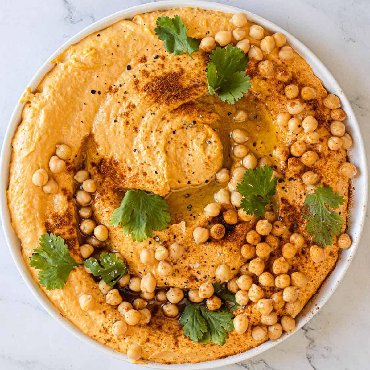 A vibrant bowl of creamy hummus served alongside perfectly roasted sweet potato wedges.  Garnished with paprika and fresh parsley.
