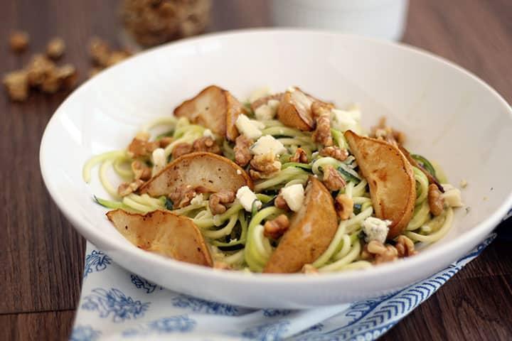 Close-up of a plate of zoodles with pears and gorgonzola, garnished with fresh herbs