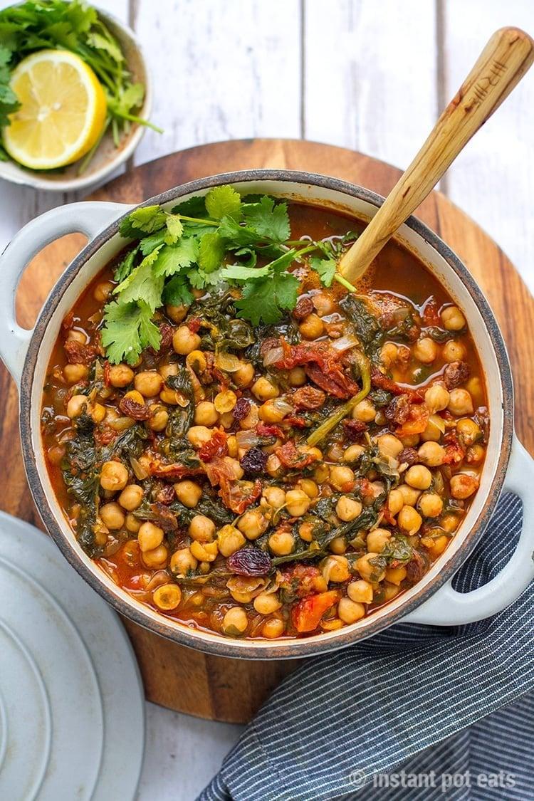 A close-up shot of a vibrant Moroccan chickpea and apricot curry simmering in a pot, with steam rising to show the warmth