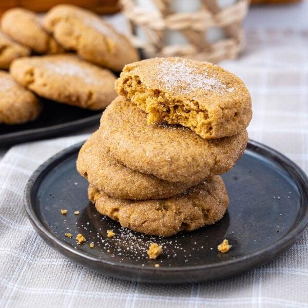 A rustic wooden table with a plate of warm peanut butter cookies, a glass of milk, and a cozy scene in the background