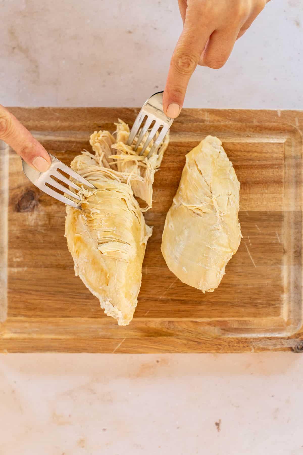 cooked chicken being shredded with two forks on a cutting board