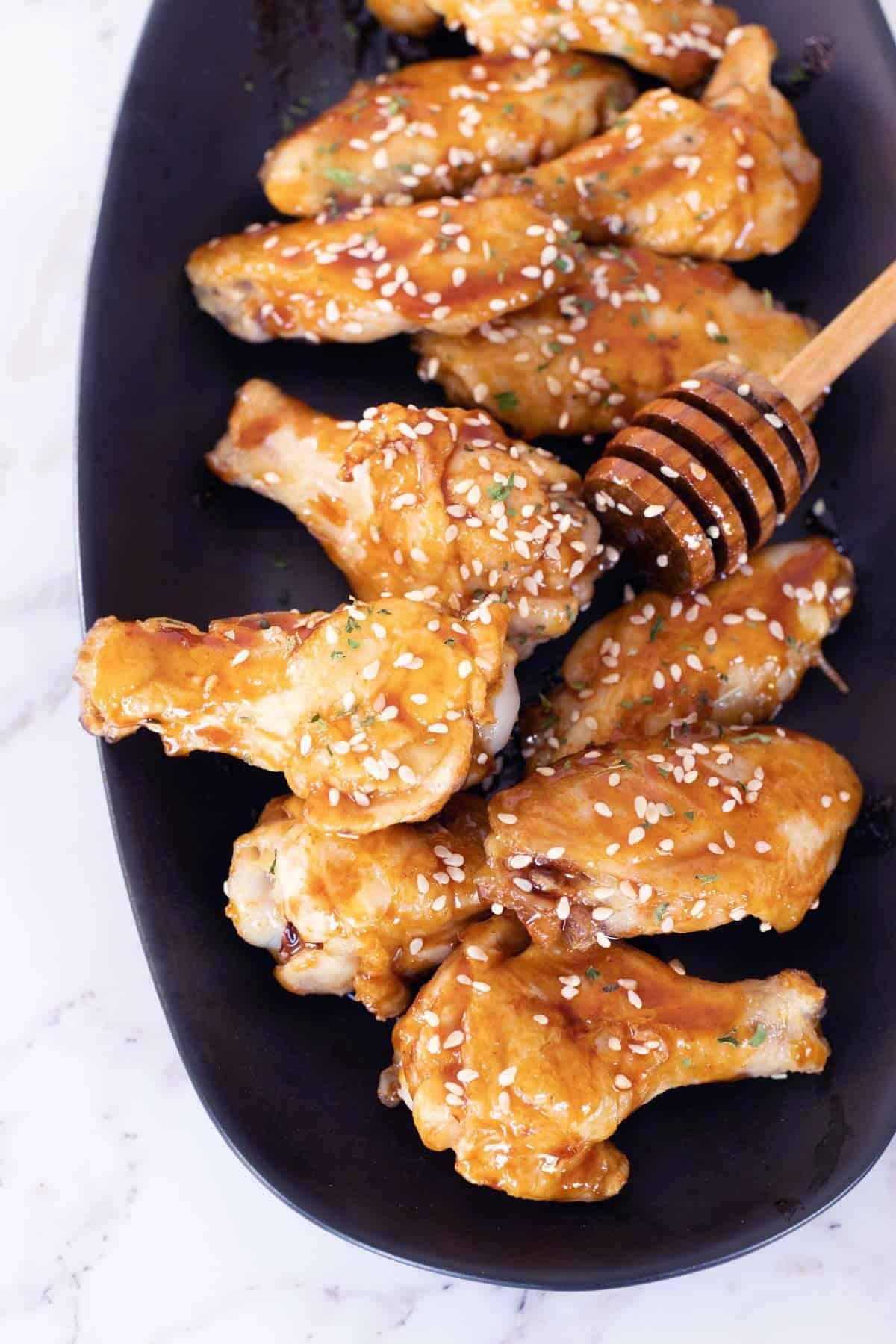 Close-up shot of golden-brown honey sriracha wings arranged on a rustic wooden platter, garnished with sesame seeds and green onions.