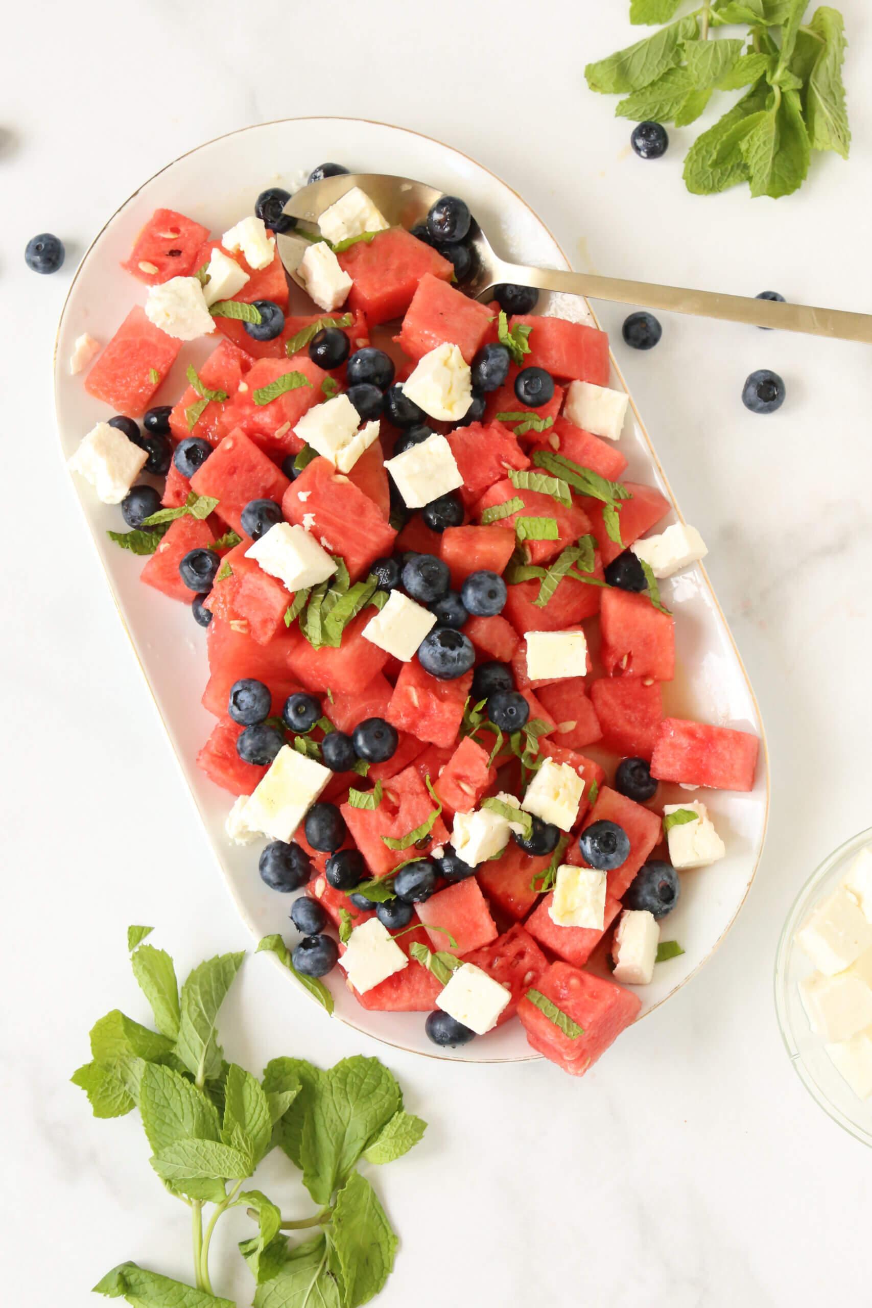 A vibrant watermelon salad with blueberries and lemon zest, garnished with fresh mint.
