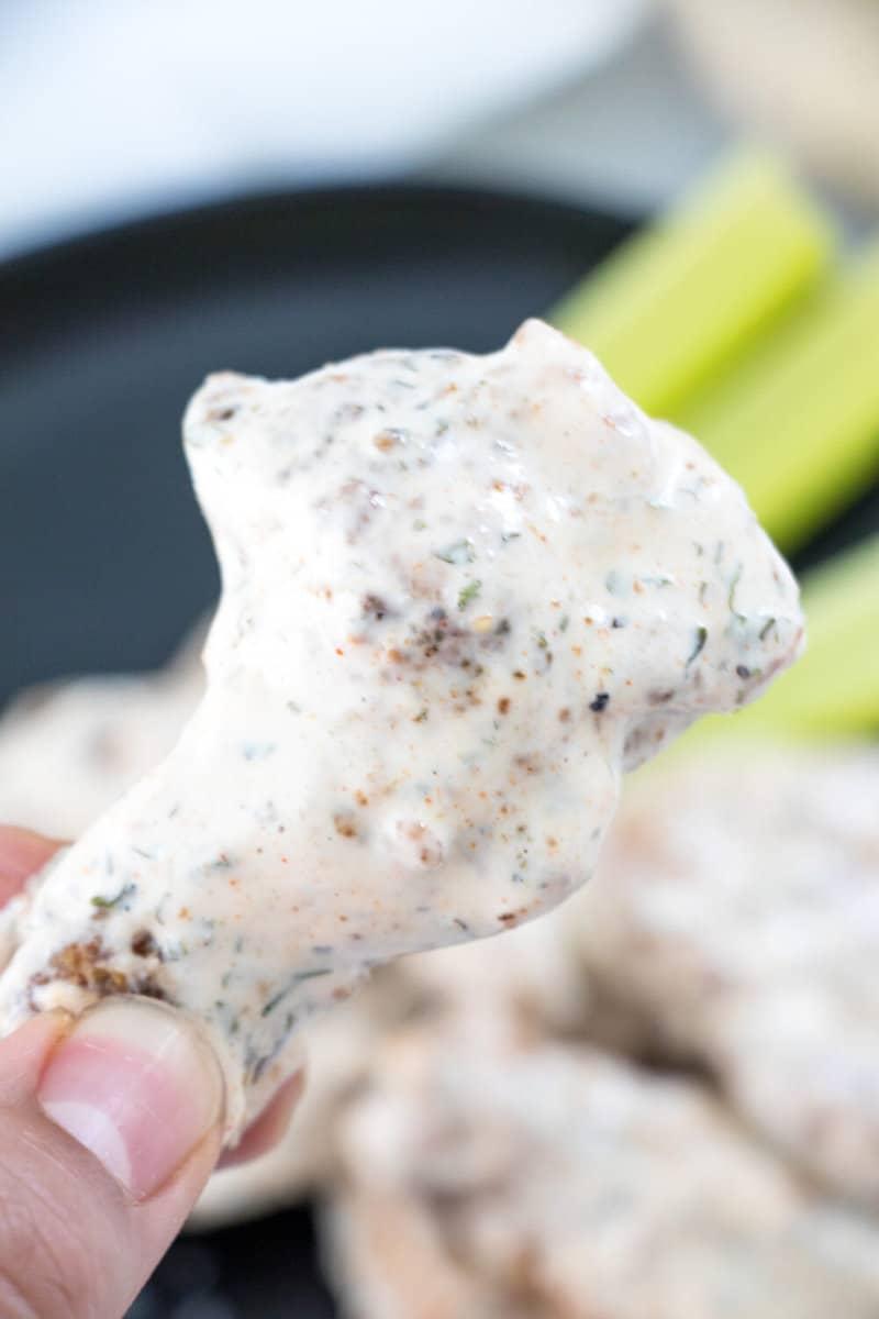 Close up of hands dipping a Cajun Ranch Wing into a bowl of ranch dressing.