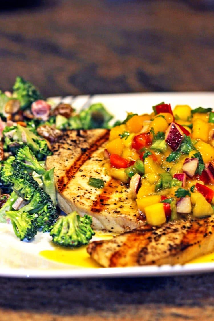 overhead shot of grilled swordfish with mango salsa on a plate, next to a grill