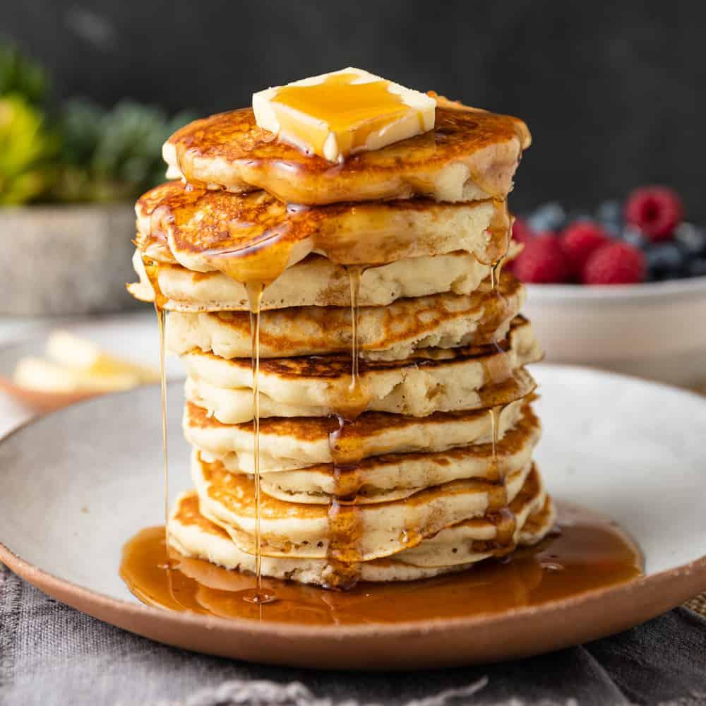 A stack of fluffy golden brown pancakes with butter and syrup