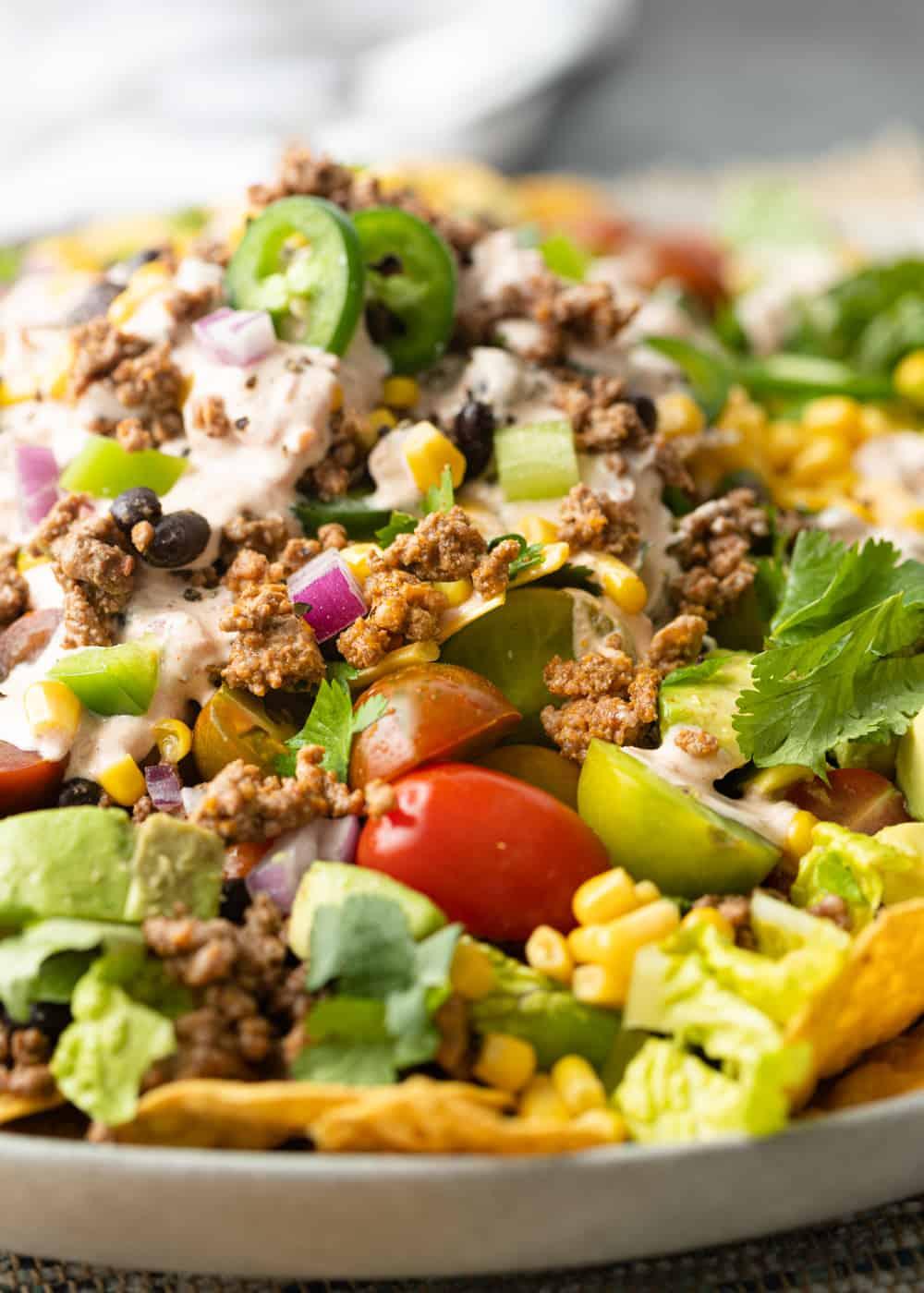 Close-up shot of a delicious taco salad with layers of ingredients, including ground beef, avocado crema, and fresh toppings