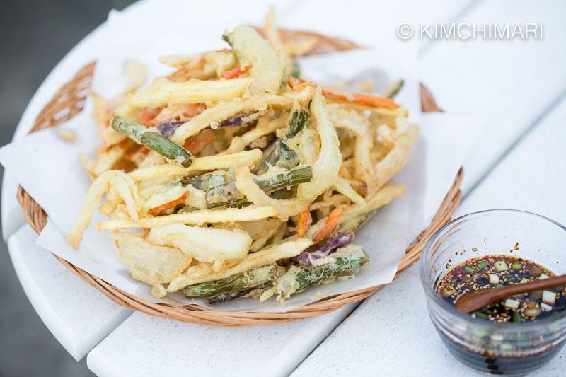 A plate of kimchi and vegetable tempura being served with various dipping sauces and side dishes